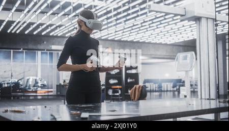 Young Female Wearing a Virtual Reality Headset and Using Controllers at Work in a Technology Research and Development Office. VR Software Developer Programming a Game or Augmented Reality Application Stock Photo