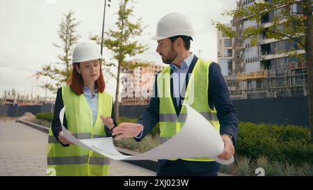 Two contractors civil engineers discuss electrical maintenance blueprint paper partnership discuss teamwork city buildings project construction Stock Photo