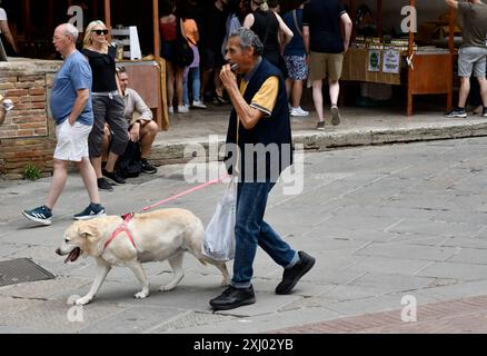 Man playing harmonica while walking his pet dog in San Gimignano in Tuscany, Italy Stock Photo