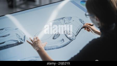 Female Car Designer Using a Digital Tablet to Draw a Prototype Car Sketch with a Stylus. Talented Industrial Artist Working in a Research and Development Studio at a Vehicle Production Factory Stock Photo