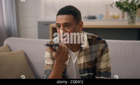 Happy African American man at home couch sofa biracial male ethnic guy using cellphone answering on audio message record voice mail recording answer Stock Photo