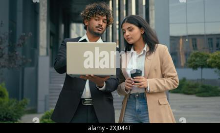 Two business colleagues talking pointing at laptop in city outdoors Arabian employees woman cooperating startup project work brainstorming looking at Stock Photo