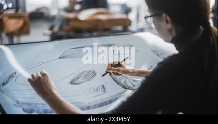 Female Automotive Designer Using a Digital Tablet to Draw a Prototype Car Sketch. Focused Industrial Artist Working in a Research and Development Studio at a Vehicle Production Factory Stock Photo