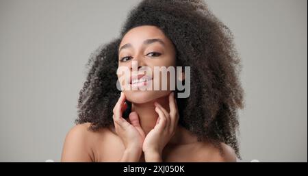 Beauty and healthcare concept - beautiful African American woman with curly afro hairstyle and clean, healthy skin looking in virtual mirror, touching Stock Photo