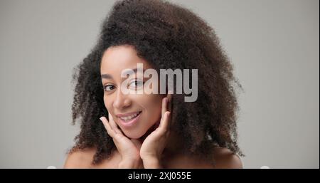 Beauty and healthcare concept - beautiful African American woman with curly afro hairstyle and clean, healthy skin looking in virtual mirror, touching Stock Photo