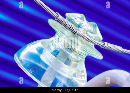 Close-up of a glass insulator wrapped with wire. The insulator is transparent and appears to be made of glass. The wire is wound around the insulator in a spiral. Stock Photo