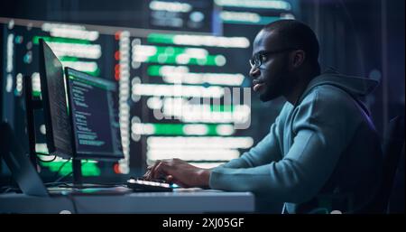 Focused Black Male Programmer Working in Monitoring Room, Surrounded by Big Screens Displaying Lines of Programming Language Code. Portrait of Man Creating Software. Futuristic Coding Concept. Stock Photo