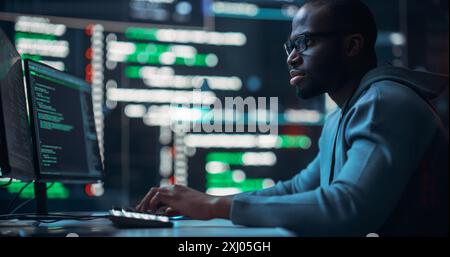 Focused Black Male Programmer Working in a Monitoring Control Room, Surrounded by Big Screens Displaying Lines of Programming Language Code. Portrait of a Man Creating a Software and Coding Stock Photo