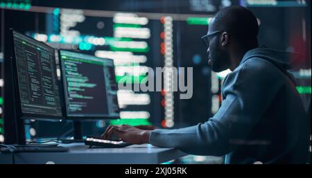 Black Male Programmer Working in Monitoring Room, Surrounded by Big Screens Displaying Lines of Programming Language Code. Portrait of Man Creating a Software. Abstract Futuristic Coding Concept Stock Photo