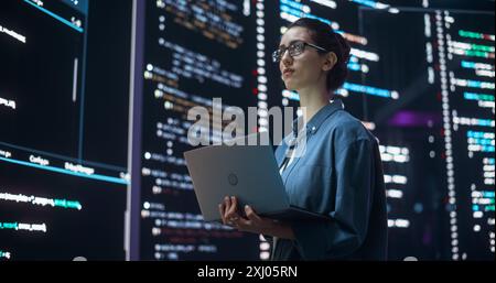Portrait of Woman Creating a Software and Coding, Surrounded by Big Screens Displaying Lines of Programming Language Code. Female Programmer Working in a Monitoring Room. Futuristic Concept Stock Photo