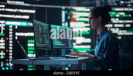 Female Developer Thinking and Typing on Computer, Surrounded by Big Screens Showing Coding Language. Professional Programmer Working in an Office, Running Coding Tests. Futuristic Programming Stock Photo