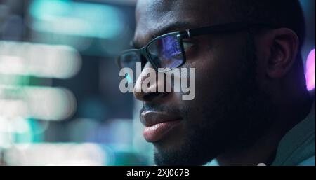 Close Up Portrait of Black Man Working on Computer, Lines of Code Language Reflecting on his Glasses. Male Programmer Developing New Software, Coding, Managing Cybersecurity Project Stock Photo