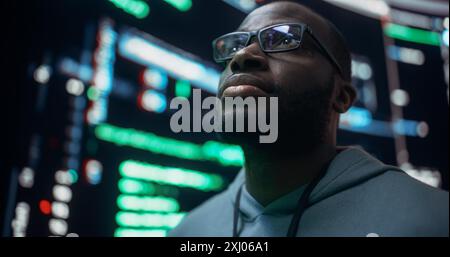 Close-Up Portrait of Young Black Man Looking at Big Digital Screens Glitching While Displaying Code. Worried Professional Programmer Fixing a Bug, Dealing with Crashing System, Thinking of Solutions. Stock Photo
