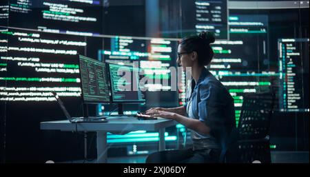 Portrait of Woman Working on Computer, Typing Lines of Code that Appear on Big Screens Surrounding her in a Monitoring Room. Female Programmer Creating Innovative Software Using AI Data and System Stock Photo