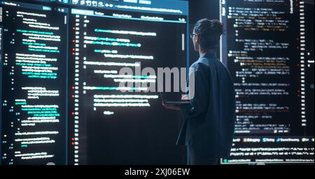 Shot of Female Programmer Working in a Monitoring Control Room, Surrounded by Big Screens Displaying Lines of Programming Language Code. Portrait of Woman Creating a Software, Coding Stock Photo