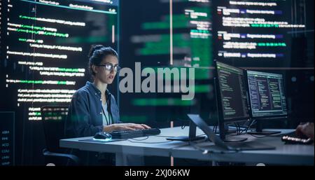 Focused Woman Working as a Developer, Surrounded by Big Screens Displaying Lines of Code in a Monitoring Room. Female Programmer Using Desktop Computer, Analysing Data, Creating AI Software Stock Photo