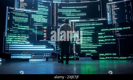 Back View of Young Black Man Walking and Looking at Big Digital Screens Glitching While Displaying Code Lines. Professional Hacker Breaking Through Cybersecurity Protection System, Changing Code Stock Photo