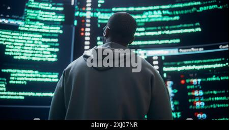 Back View of Young Black Man Looking at Big Digital Screens Glitching While Displaying Code Prompts. Worried Professional Programmer Fixing a Bug, Dealing with Crashing System, Ensuring Cybersecurity Stock Photo