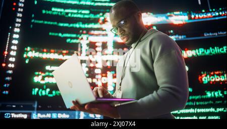 Portrait of Young Black Man Working on Laptop Computer, Looking at Big Digital Screens Glitching While Displaying Code Lines. Professional Programmer Fixing Software Bug, Dealing with Crashing System. Stock Photo