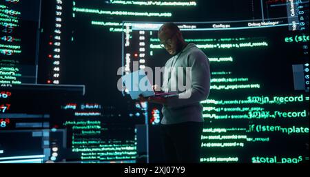 Portrait of Young Black Man Working on Laptop Computer, Looking at Big Digital Screens Glitching While Displaying Code Lines. Professional Programmer Fixing a Bug, Dealing with Crashing System Stock Photo