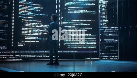 Portrait of Young Woman Working on Laptop Computer, Looking at Big Digital Screen Displaying Back-end Code Lines. Professional Programmer Developing a Big Data Interface Software Project Stock Photo