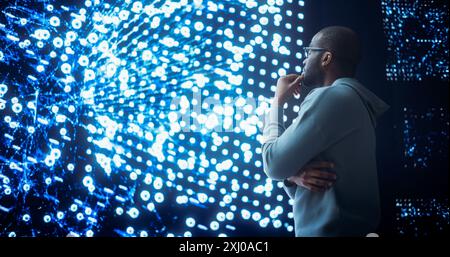 Black Young Man Looking at a Big Screen with Neural Network Visualisation In 3D. Professional Computer Data Science Engineer Working in System Control and Monitoring Telecommunications Office Stock Photo