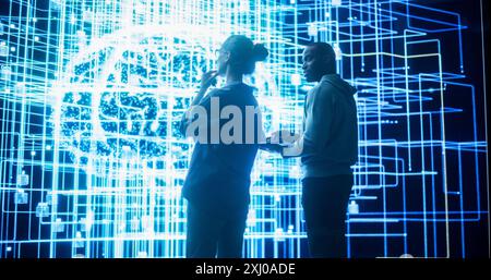 Portrait of Two Diverse Colleagues Looking at a Big Screen with Neural Network 3D Visualisation. Professional Computer Data Scientists Discussing and Working on Monitoring Private Information Stock Photo