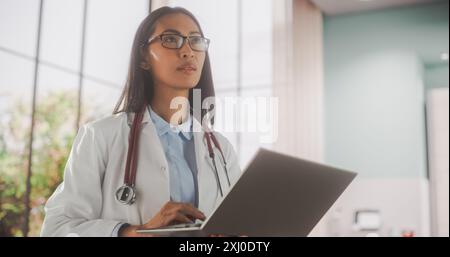 Portrait of a Medical Health Care Professional Using a Laptop Computer in Hospital Office. Asian Clinic Physician in White Coat Appointing Prescriptions Online, Updating Electronic Health Records Stock Photo
