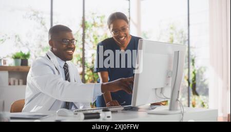 Health Care Medical Hospital. Happy African American Nurse and Black Doctor Having a Casual Conversation, Using Desktop Computer, Laughing and Smiling During a Break at Work Stock Photo