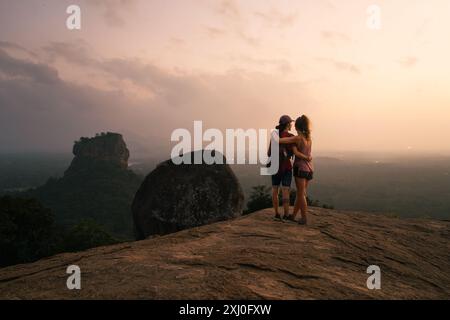 Couple standing on a rock and enjoying a breathtaking view of Sigiriya Rock in Sri Lanka during sunset. Stock Photo