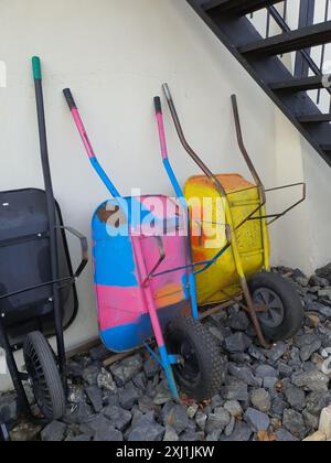 Colorful painted wheelbarrows leaning against white wall under staircase Stock Photo