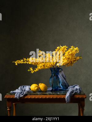 Branches of yellow flowers on a marble wooden table. Nearby are two lemons and a blue handkerchief. Dark gray background. spring still life. Vitamins. Stock Photo