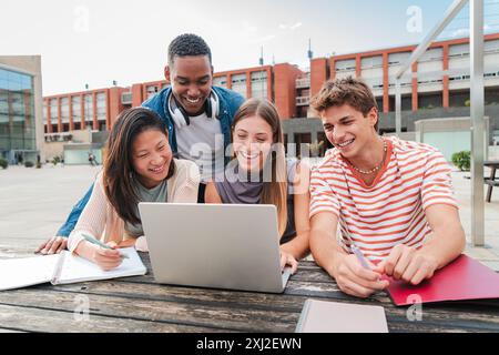 Teamwork of teenage students using a laptop to prepare a exam. Group of classmates learning together with a notebook on the university campus after class. Highschool people brainstorming and talking. High quality photo Stock Photo