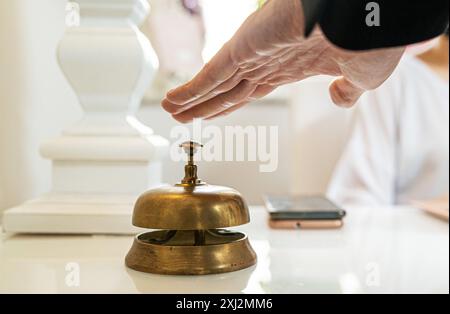 Close-up of hotel reception desk featuring antique brass service bell. Guest's hand reaching to ring for assistance, symbolizing luxury hospitality an Stock Photo