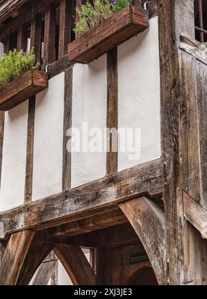 An historic half-timbered building. A door sits under a gallery and a stairway runs up the side. Planters are filled with flowers. Stock Photo