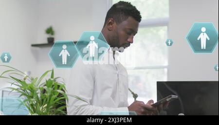 Image of profile icons floating against african american man using digital tablet at office. Global networking and business technology concept Stock Photo