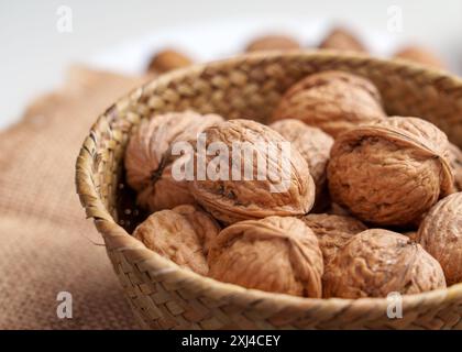 Whole walnuts in wooden rattan bowl, their shells showing intricate patterns and textures. They are ready to be cracked open, revealing the delicious Stock Photo
