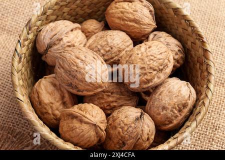 Organic unshelled walnuts as a source of protein and fiber in a rustic wicker bowl on rough burlap. Whole nutritious nuts. Top view Stock Photo