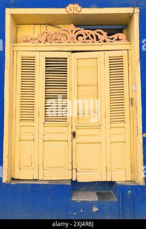 516 One-storey Colonial townhouse of peach-yellow painted wood door with louvered shutter on azure-blue facade, Calle Heredia Street. Santiago-Cuba. Stock Photo