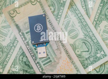 A dark blue USB hardware wallet with a Bitcoin logo on a background of US dollar bills, in South Korea Stock Photo