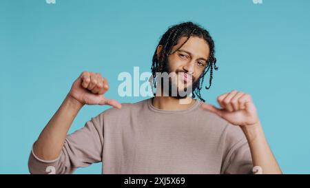 Upset Middle Eastern man showing thumbs down sign gesturing, disapproving, offering negative feedback. Disappointed BIPOC person doing rejection hand gesture, studio background, camera B Stock Photo