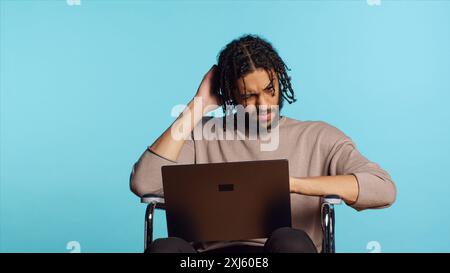 Middle Eastern man composing email, typing on laptop keyboard, struggling to think of what to write. BIPOC person sending mail online, brainstorming message idea, studio background, camera A Stock Photo