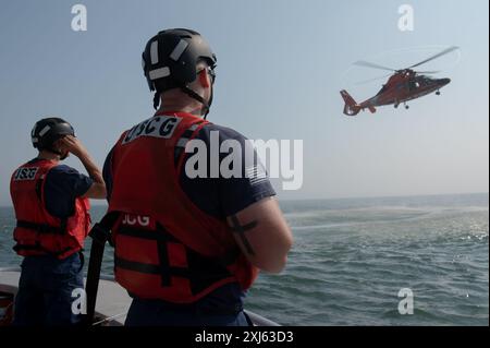 From left, U.S. Coast Guard Academy Cadet 3rd Class Ben Bonetto and Petty Officer 2nd Class Charles Weaver, a crew member at U.S. Coast Guard Station Barnegat Light, anticipate a rescue basket delivery from an Air Station Atlantic City MH-65D Dolphin helicopter off Barnegat Light, New Jersey in the North Atlantic Ocean, July 15, 2024. Bonetto and Weaver conducted training with two separate MH-65 Dolphin crews from Air Station Atlantic City during the operation. (U.S. Coast Guard photo by Petty Officer 3rd Class Christopher Bokum) Stock Photo