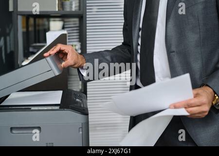 Unrecognizable businessman in grey suit opening lid of xerox machine after making copy of juridical or financial papers in office Stock Photo