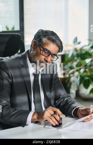 Confident mature male notary in formalwear stamping signed paper documents while preparing for visit of clients Stock Photo