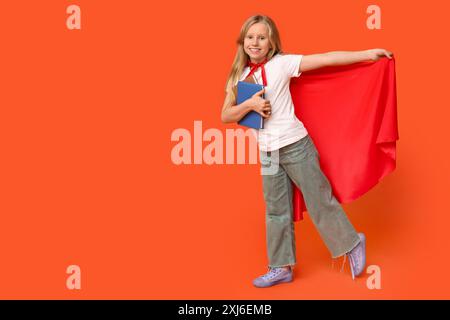 Cute teenage girl dressed as superhero with books on orange background. Library Lovers Day Stock Photo