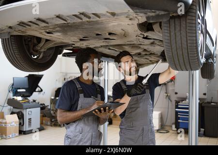 Two mechanics check vehicle chassis on lift in garage Stock Photo