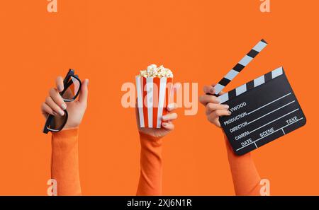 Three womans hands holding clapperboard, popcorn and 3d glasses on an orange background Stock Photo