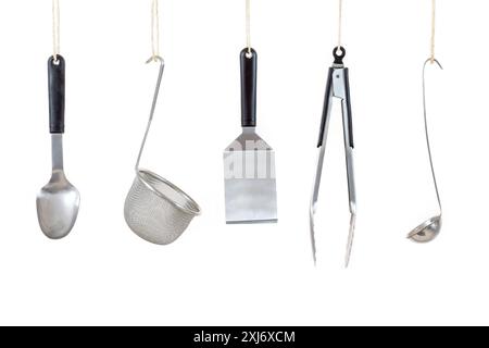 Row of stainless steel cooking implements hanging on a white background Stock Photo