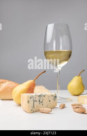 Close up view of dorblu cheese, wine glass, pears, almond and baguette on gray Stock Photo